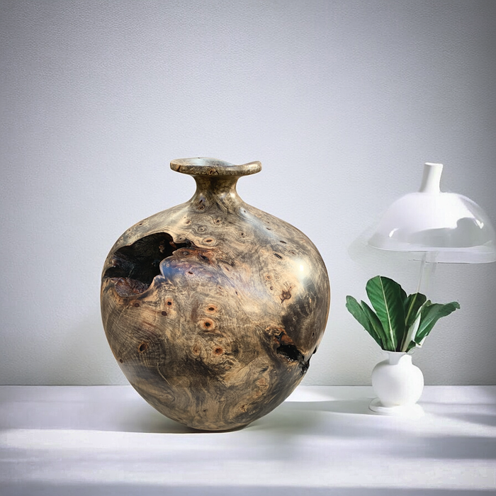 A large elegant wood vase in buckeye burl resting on a table in a white contemporary setting