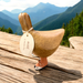 Wood duck wearing pink and black doggy boots standing on a wooden table while viewing lush green mountains.