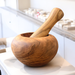 wooden mortar displayed on a white counter top of a pharmacy with white walls. Mortars and pestles is a tool that's often used in compound pharmacies to crush tablets.