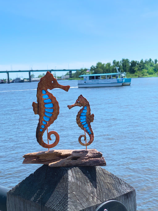 Wooden seahorses with blue epoxy accent sit atop a rustic wooden base facing each other on the Cape Fear River.